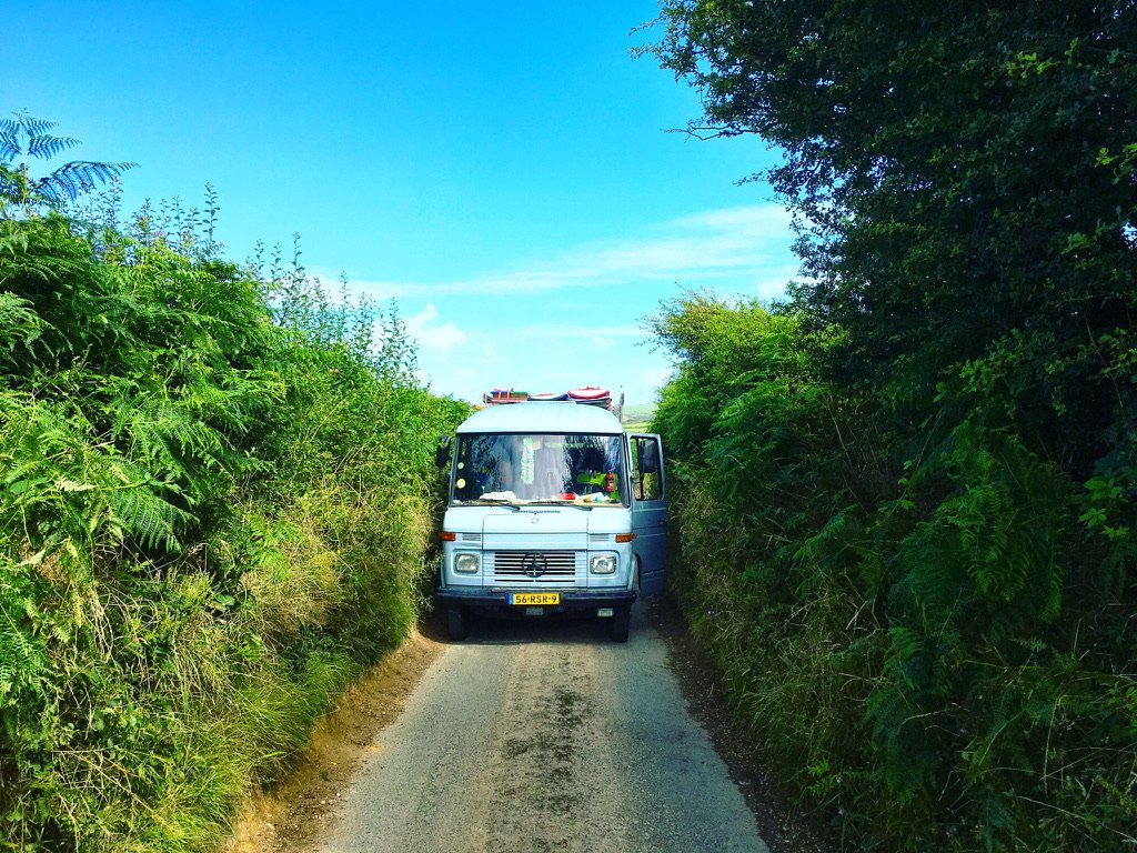 vintage blauwe camper op smalle weg omgeven door bos