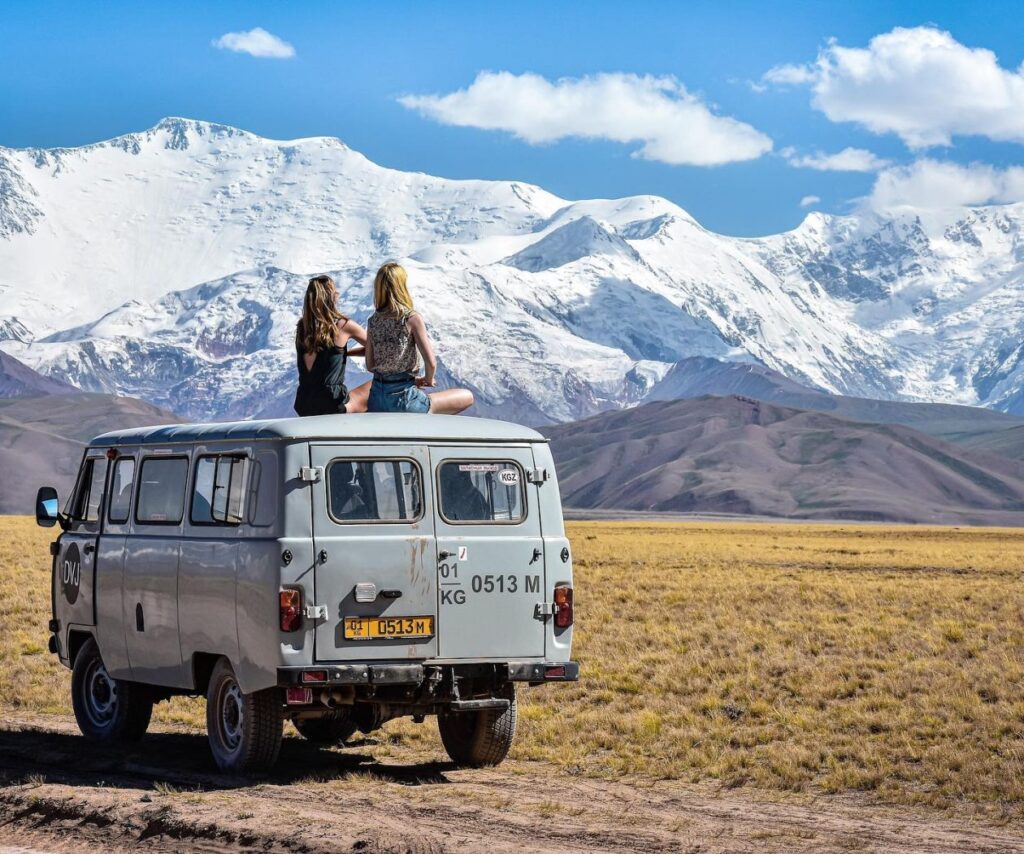 grijs busje met twee vrouwen erop die kijken naar de bergen in de verte