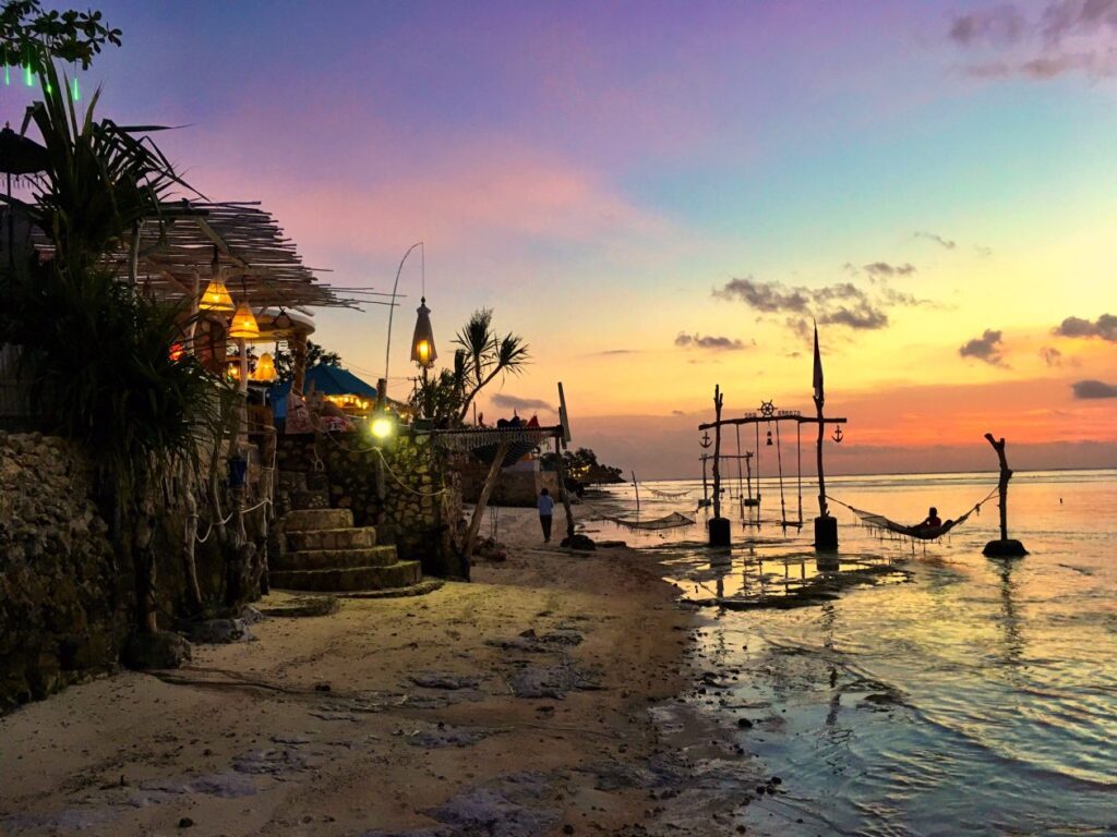 Zonsondergang met links strand met een hangmat rechts het donkere silhouet van een restaurant