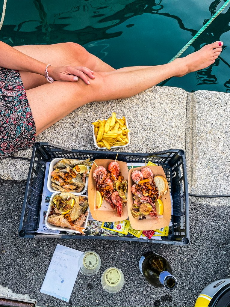 twee vrouwen benen aan een kade met gefrituurde vis in een kistje