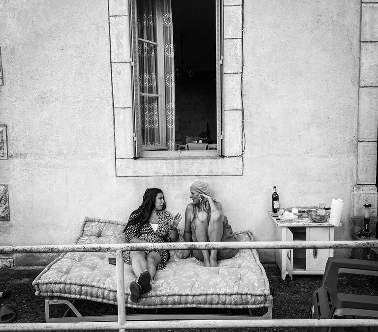 twee vrouwen buiten op een bed tegen een huis aan