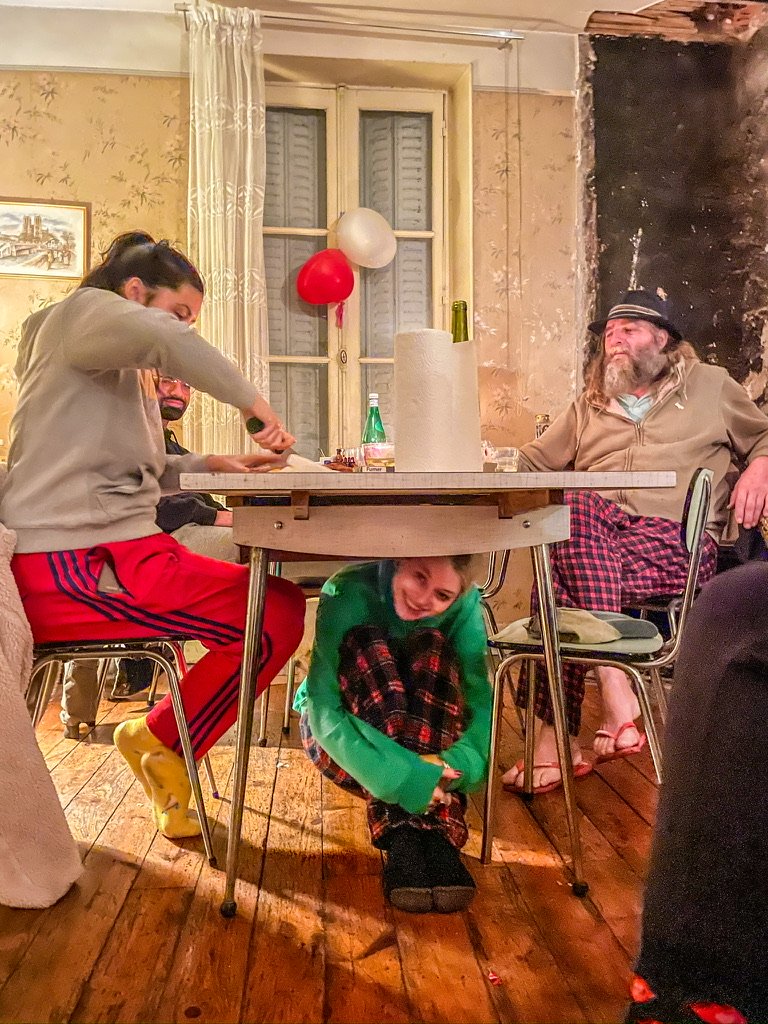 Meisje onder eettafel in groen T-shirt met twee mensen links en rechts aan de tafel zittend