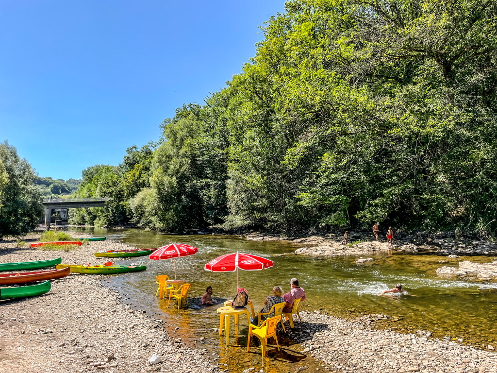 terras van gele stoelen en tafels in een rivier met bomenrij aan de rechter kant