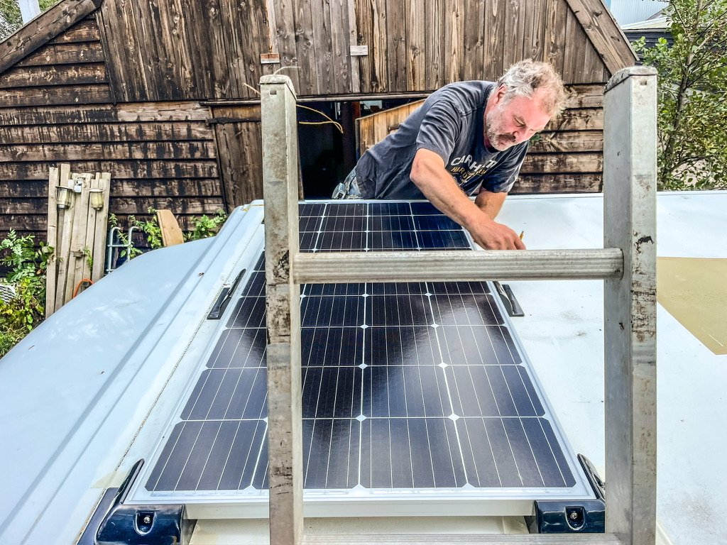 man op trap installeert zonnepanelen op bus
